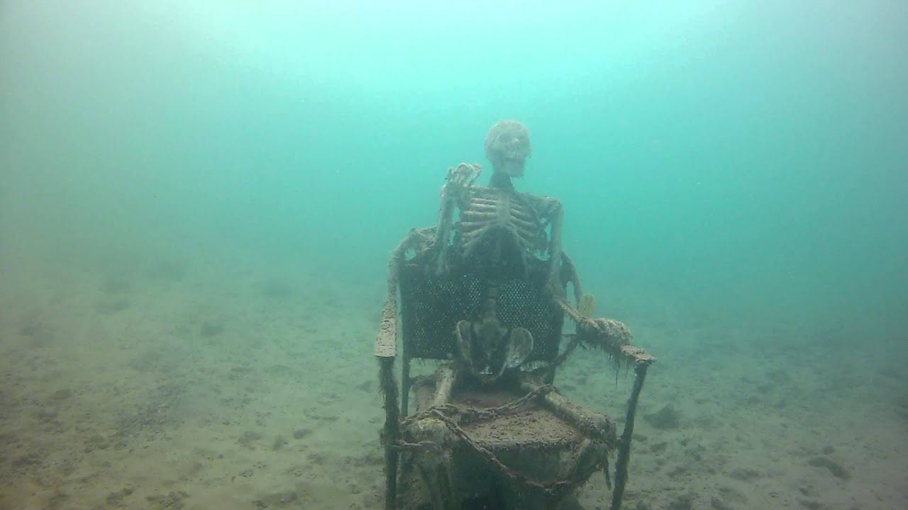 A skeleton sitting in a chair at the bottom of the sea